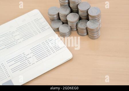 Primo piano di una pila instabile di monete d'argento sul libretto bancario. Foto Stock