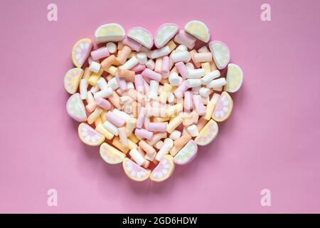 Marshmallow multicolore a forma di cuore su sfondo rosa. Vista dall'alto Foto Stock