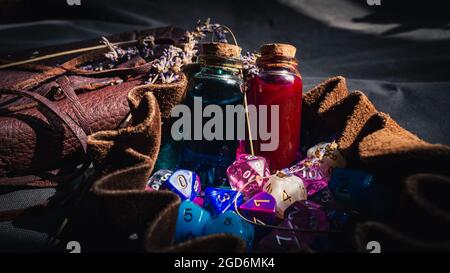 Immagine ravvicinata di due bottiglie di pozione, un notebook in pelle, una borsa per dadi in pelle marrone con dadi RPG alla luce del sole Foto Stock