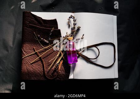 Immagine a soffitto di una bottiglia con tappo in vetro con liquido rosa e lavanda secca sopra un notebook marrone aperto con rilegatura in pelle. Foto Stock