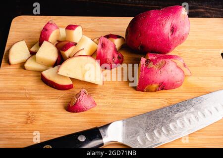 Tagliando patate rosse in un tagliere di bambù: Tagliando patate rosse in pezzi di dimensione morso su un tagliere di legno Foto Stock