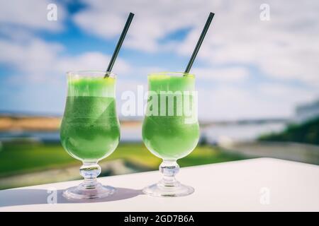 I frullati verdi disintossano mangiare sano succo di pulizia succhi di frutta al caffè. Dieta vegetariana tendenza alla spremitura. Due bicchieri di succo di verdure di spinaci all'aperto Foto Stock