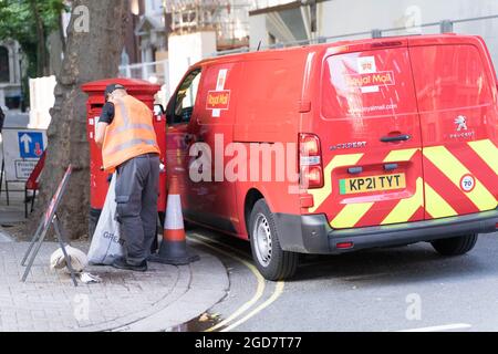 Posta l'uomo che raccoglie le lettere dalla scatola postale e il pulmino reale della posta sulla via di Londra, Inghilterra Foto Stock