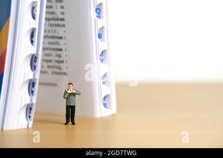 Foto di personaggi giocattolo in miniatura. Libreria di concetto. Un uomo in piedi di fronte al dizionario aperto libro. Foto immagine Foto Stock