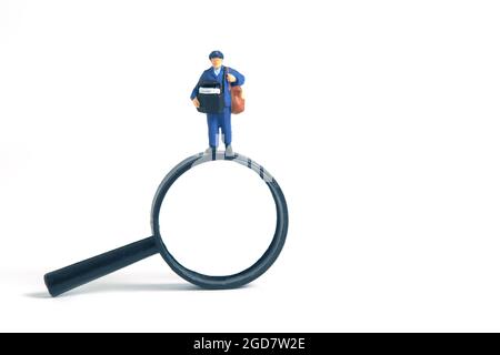 Fotografia concettuale dei giocattoli delle persone in miniatura. Ricerca della posizione dell'indirizzo. Corriere Postman con lente di ingrandimento, isolato su sfondo bianco. Foto Stock