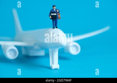 Fotografia concettuale dei giocattoli delle persone in miniatura. Consegna pacchi in aereo. Corriere di posta con piano bianco, isolato su sfondo blu. Foto Stock
