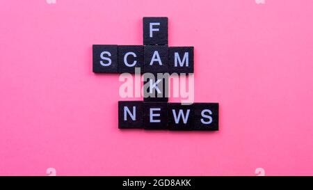 Un gruppo di piastrelle scrable che formano le notizie false di truffa di parola. Fuoco selettivo sulle piastrelle isolate su sfondo rosa Foto Stock