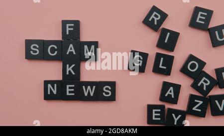 Un gruppo di piastrelle scrable che formano le notizie false di truffa di parola. Fuoco selettivo sulle piastrelle isolate su sfondo rosa Foto Stock