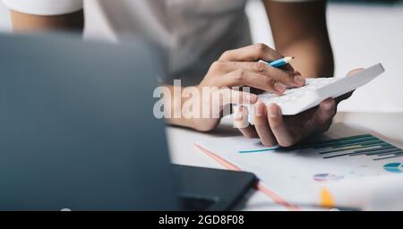 Primo piano mano del contabile che lavora sulla scrivania del luogo di lavoro in ufficio calcolatore d'uso calcola le spese mensili, le tasse, il saldo del conto corrente bancario Foto Stock