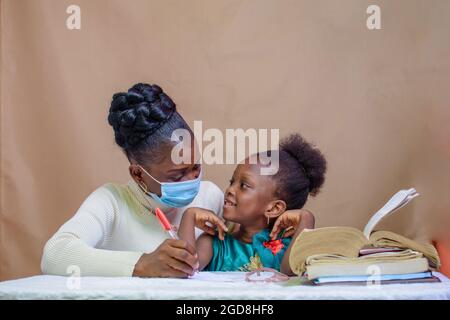 Insegnante o madre africana con maschera al naso, insegnando e aiutando una bambina con i suoi studi per eccellere nella scuola, nell'istruzione e nella carriera Foto Stock