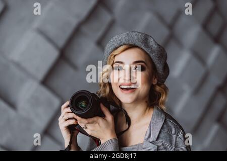 Ritratto di una bella fotografa donna di stile in un vestito grigio con una macchina fotografica in mano in uno studio fotografico. Messa a fuoco selettiva morbida. Spazio di copia. Foto Stock