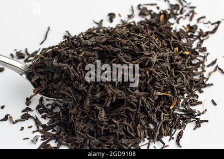 Foglie di tè Assam essiccato su cucchiaio d'argento su sfondo bianco. Foto Stock