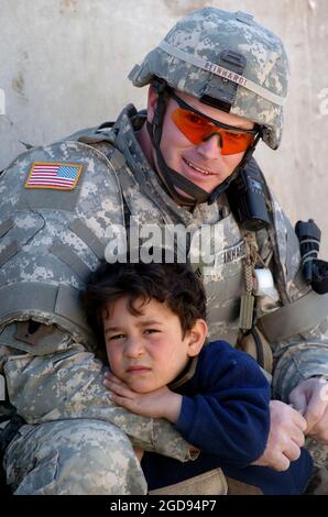 US Army (USA) Corporal (CPL) James Reinhard, VIPES Task Force (TF), sede centrale/distaccamento della sede centrale (HHD), 519th Military Police (MP) Company (MP Co), comforts 5 anni Okmed fuori di una stazione di polizia irachena (IP) a Baghdad, provincia di Baghdad, Iraq (IRQ), Mentre si prende una pausa dalla formazione e l'assistenza di IP ufficiali durante l'operazione LIBERTÀ IRACHENA. (FOTO US NAVY DI PH1 (AW) BART A BAUER 060312-N-7586B-202) Foto Stock