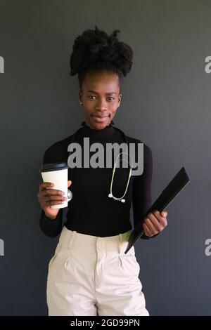 Giovane studentessa africana di medicina con stetoscopio, cartelle e un caffè. Foto Stock