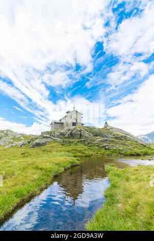 Piccola cappella che si riflette in acque pulite del torrente di montagna in estate, Alpe Pradello, Valmalenco, Valtellina, Lombardia, Italia Foto Stock