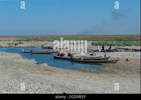 Al-Chibayish, Iraq. 1 novembre 2018 pescatori arabi paludosi con le loro canoe Mashoof ormeggiate al bordo della terra secca cracked della marsetta centrale Foto Stock