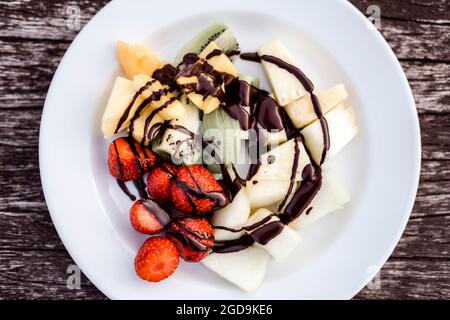 Deliziosa Macedonia di frutta con condimento al cioccolato su panca di legno Foto Stock