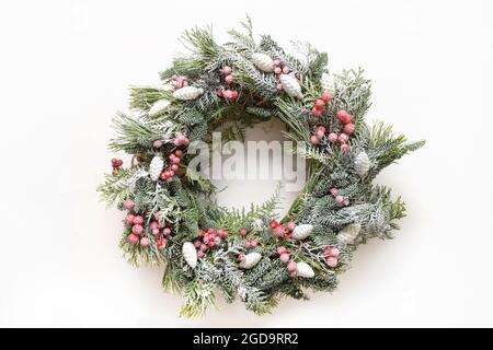 Corona di Natale di rami freschi sempreverdi naturali con decorazioni rosse e bianche al centro di sfondo bianco. Biglietto di auguri per il nuovo anno. Vista dall'alto. T Foto Stock