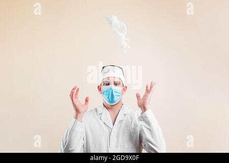 Giovane medico ritratto in bianco camice da laboratorio maschera protettiva di respirazione getta giù guanti bianchi su sfondo giallo isolato. Messa a fuoco selettiva. Foto Stock