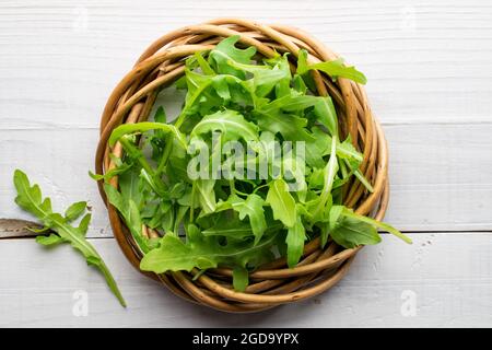 Succosa verde organico sprigs di rucola con una corona di vite, primo piano, su un tavolo di legno, vista dall'alto. Foto Stock