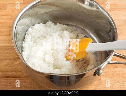 Paletta con porridge di riso su sfondo di legno. Mescolare con un cucchiaio di silicone Foto Stock