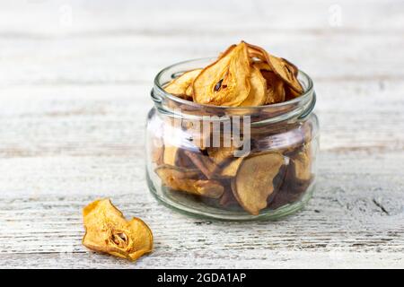 Un mucchio di fette secche di pere in vaso di vetro su sfondo bianco di legno. Patatine di frutta secca. Cibo vegano sano Foto Stock