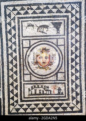 Testa di Medusa emblema mosaico bianco e nero in opus vermiculatum realizzato in tessere policromi. La testa di Medusa è raffigurata nel tondo centrale che è inserito in un pannello con quadrati negli angoli. Altri due campi rettangolari contengono una città murata con una palma e una torre nella parte inferiore e un faro con due navi nella parte superiore. Le scene sono racchiuse all'interno di due cornici con triangoli neri a contrasto, delimitati da altri fotogrammi lineari. Pompei, Casa del Centenario - prima metà del i secolo d.C. Foto Stock