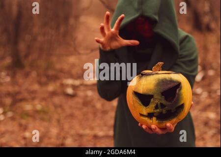 Una strega creepy tiene una zucca fumante in una foresta profonda. Jack o lanterna emette fumo giallo per Halloween Foto Stock