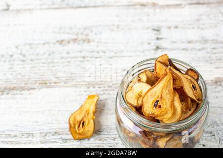 Un mucchio di fette secche di pere in vaso di vetro su sfondo bianco di legno. Patatine di frutta secca. Cibo vegano sano Foto Stock