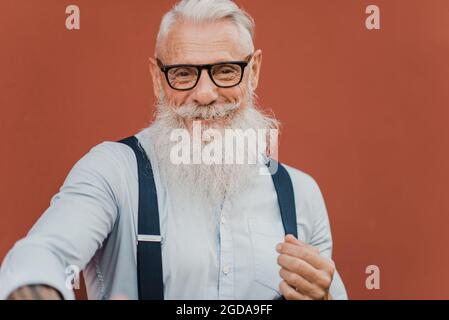 Uomo anziano felice che guarda la macchina fotografica che indossa abiti e occhiali moderni Foto Stock