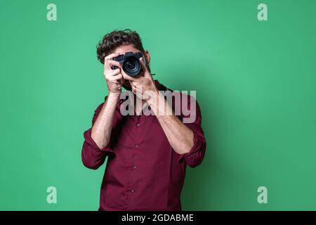 Ragazzo che tiene una macchina fotografica mirrorless e che fa una foto mentre guarda attraverso il mirino elettronico. Foto Stock