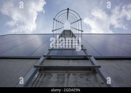 Fuga dal fuoco sull'edificio industriale sopra, vista dal basso. Corrimano in acciaio inox, scala per tetti. Vista in dettaglio delle scale con gabbia di sicurezza. Edificio con co Foto Stock