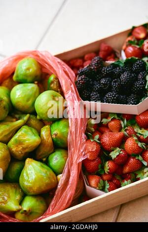 Scatola con fragole, more, fichi giace su una piastrella Foto Stock