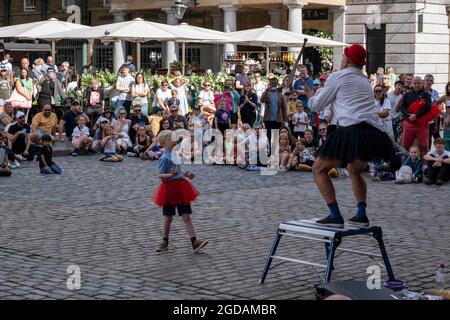 Con molte persone e famiglie che soggiornano nel Regno Unito per la loro pausa estiva durante le vacanze scolastiche, un gran numero di turisti nazionali, Chi di solito ha viaggiato all'estero, ha deceduto sulla capitale per vedere le attrazioni, come visto qui a Covent Garden, dove la gente si è riunita per guardare gli artisti di strada nella piazza il 10 agosto 2021 a Londra, Regno Unito. A seguito del Coronavirus / Covid-19 salute paura degli ultimi due anni, e con alcune restrizioni di viaggio ancora in vigore, più persone hanno scelto una staycation che è una vacanza trascorsa in un paese di origine piuttosto che abro Foto Stock
