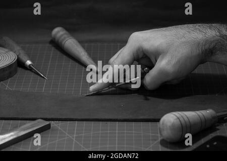 Scala di grigi primo piano di una mano dell'uomo che lavora con un attrezzo per la lavorazione della pelle. Foto Stock