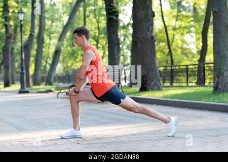 L'uomo atletico tiene la posizione di affondo. Allungamento delle gambe post-allenamento. Routine di allungamento Foto Stock