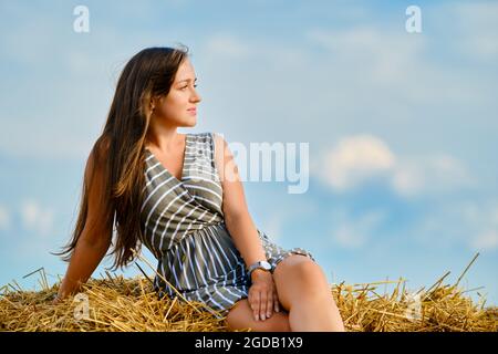 Il closeup della giovane donna siede sulla parte superiore della pila di paglia sul campo Foto Stock