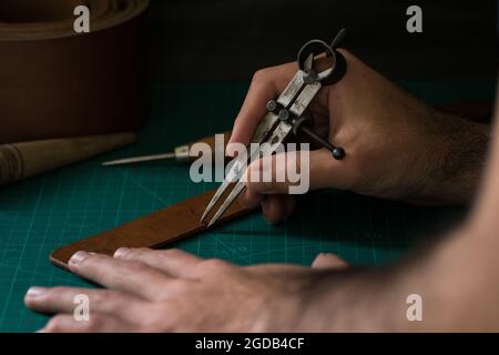 Primo piano delle mani di un uomo che lavora con un attrezzo per la lavorazione della pelle. Foto Stock