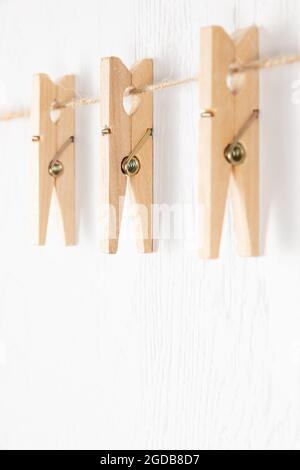 tre clothespins di legno con una molla di metallo appendono su una corda su uno sfondo bianco. fuoco selettivo Foto Stock