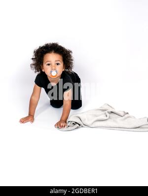 Ritratto verticale di una razza mista di 2 anni e mezzo ragazzo succhiando un capezzolo mentre strisciando Foto Stock
