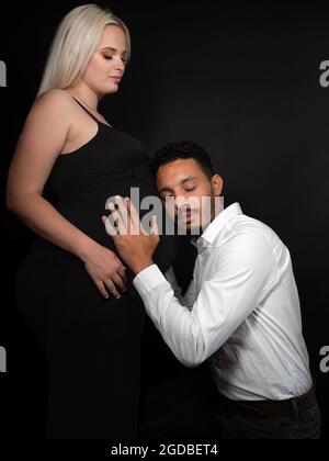 Razza mista padre-essere ascoltare la pancia della sua moglie caucasica incinta Foto Stock