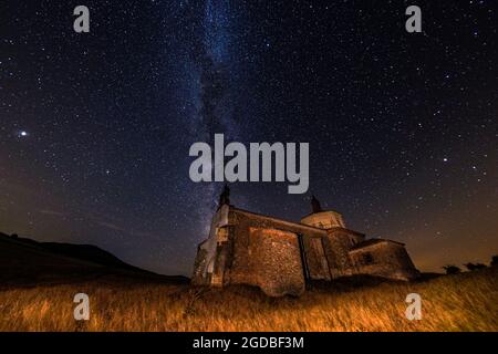 Immagine notturna di un antico eremo illuminato con un cielo stellato e la via lattea in un campo di grano Foto Stock