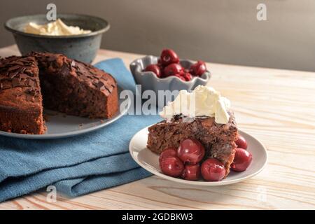 Torta rustica al cioccolato con ciliegie di morello e panna montata su un tovagliolo blu e un tavolo di legno, spazio copia, fuoco selezionato Foto Stock