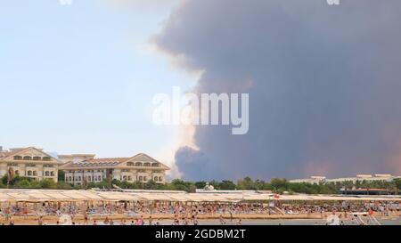Fumo da incendi boschivi che si innalzano su una spiaggia ad Antalya, Manavgat località della Turchia. Vista con la gente sulla spiaggia: Antalya, Manavgat Turchia - luglio Foto Stock