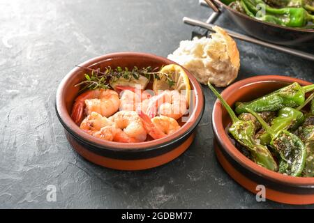 Tapas spagnole in ciotole tradizionali, pimientos fritti o peperoni e gamberi con limone ed erbe su uno sfondo grigio ardesia, copia spazio, selecte Foto Stock