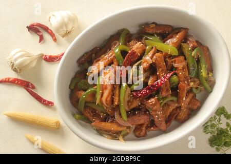 Baby mais manchurian. Croccante mais fritto in salsa manchuriana con peperoni e cipolle. Scatto su sfondo bianco Foto Stock