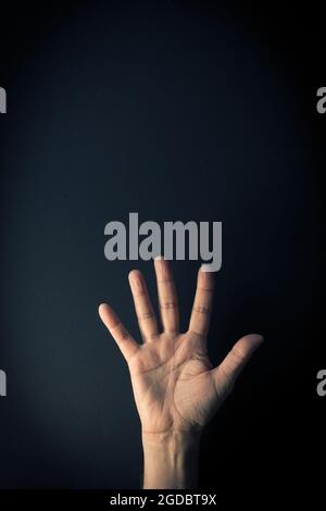 Immagine a colori drammatica della mano maschile che dimostra il linguaggio dei segni numero cinque su sfondo scuro con spazio vuoto per i redattori Foto Stock
