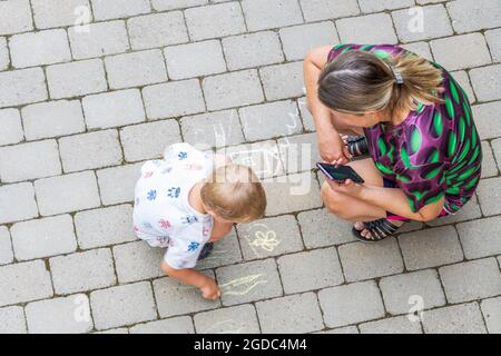 Vista dall'alto sul disegno di bambini su lastre di pavimentazione e donna che lo guarda. Svezia. Foto Stock