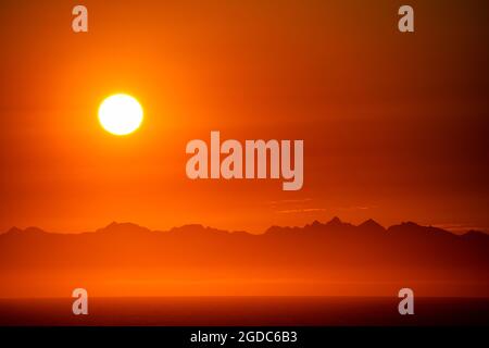 Bellissima alba del cielo arancione sulle montagne in mare Foto Stock