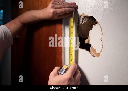 Le mani misurano il foro nella parete asciutta danneggiata Foto Stock